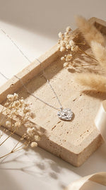 Lundholm My Monica Serie ketting dames zilverkleurig met gehamerd hartje hanger lifestyle op travertijn steen met droogbloemen - waterproof premium stainless steel sieraden cadeau vrouw moederdag verjaardag Scandinavisch Design