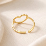 Lundholm My Rae goudkleurige verstelbare statement ring voor dames met open hart ontwerp en gestippeld textuur, gefotografeerd op crème zijde voor elegante productshot. Premium stainless steel met PVD gold plating van 2.5 micron, waterproof en hypoallergeen. Een romantisch cadeau voor vrouw, moeder of vriendin op Moederdag of verjaardag in Scandinavisch design.