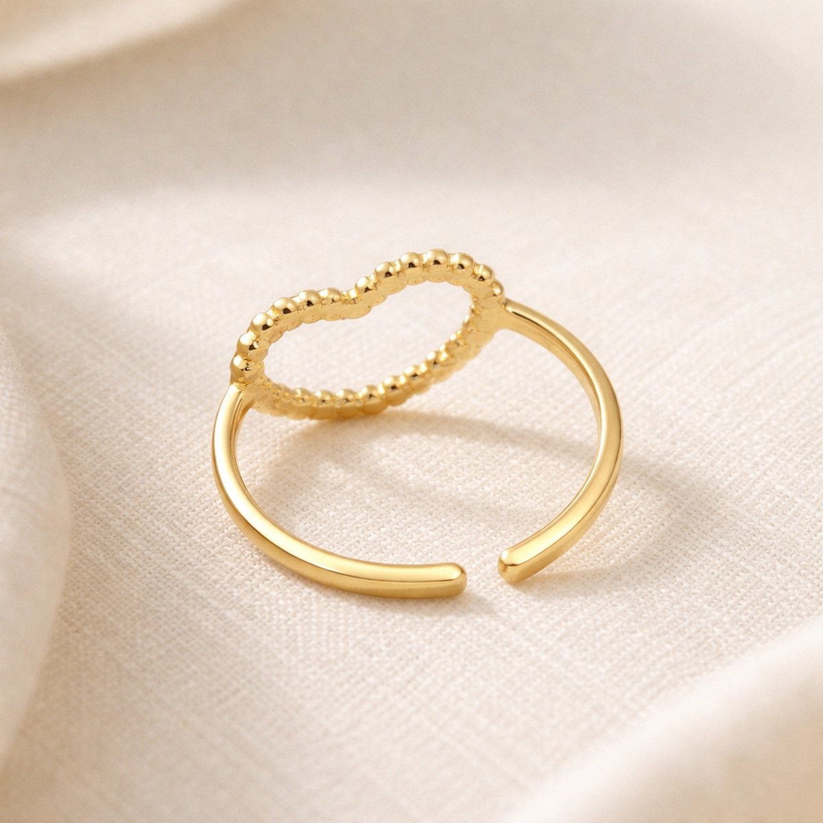 Lundholm My Rae goudkleurige verstelbare statement ring voor dames met open hart ontwerp en gestippeld textuur, gefotografeerd op crème zijde voor elegante productshot. Premium stainless steel met PVD gold plating van 2.5 micron, waterproof en hypoallergeen. Een romantisch cadeau voor vrouw, moeder of vriendin op Moederdag of verjaardag in Scandinavisch design.