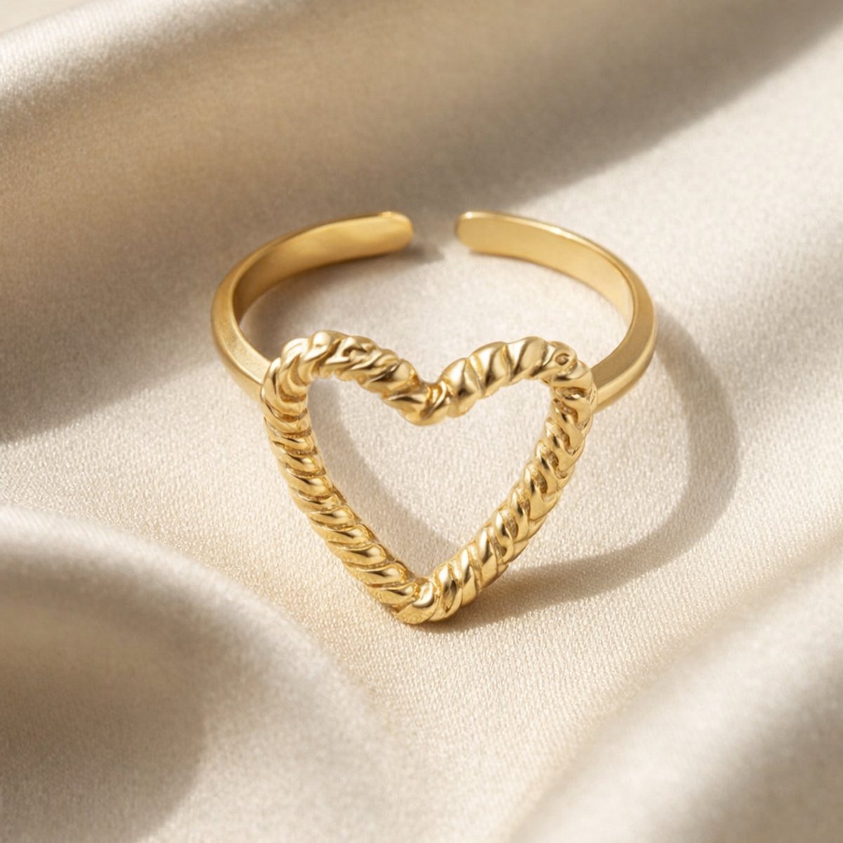 Lundholm My Rae goudkleurige verstelbare statement ring voor dames met open hart ontwerp en getwiste touw textuur, gefotografeerd op crème zijde voor stijlvolle productshot. Premium stainless steel met PVD gold plating van 2.5 micron, waterproof en hypoallergeen. Een romantisch cadeau voor vrouw, moeder of vriendin op Moederdag of verjaardag in Scandinavisch design.