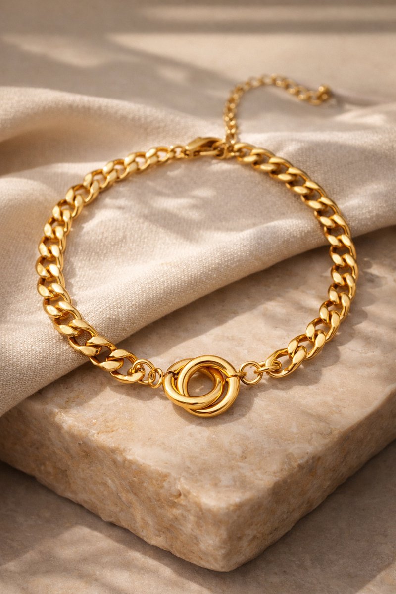 Lundholm My Tilda goudkleurige schakelarmband voor dames van 16,4 cm met verbonden ringen detail, gefotografeerd op crème stof en travertijn steen voor warme productshot. Premium stainless steel met PVD gold plating van 2.5 micron, waterproof en hypoallergeen. Een tijdloos cadeau voor vrouw, moeder of vriendin op Moederdag of verjaardag in Scandinavisch design.