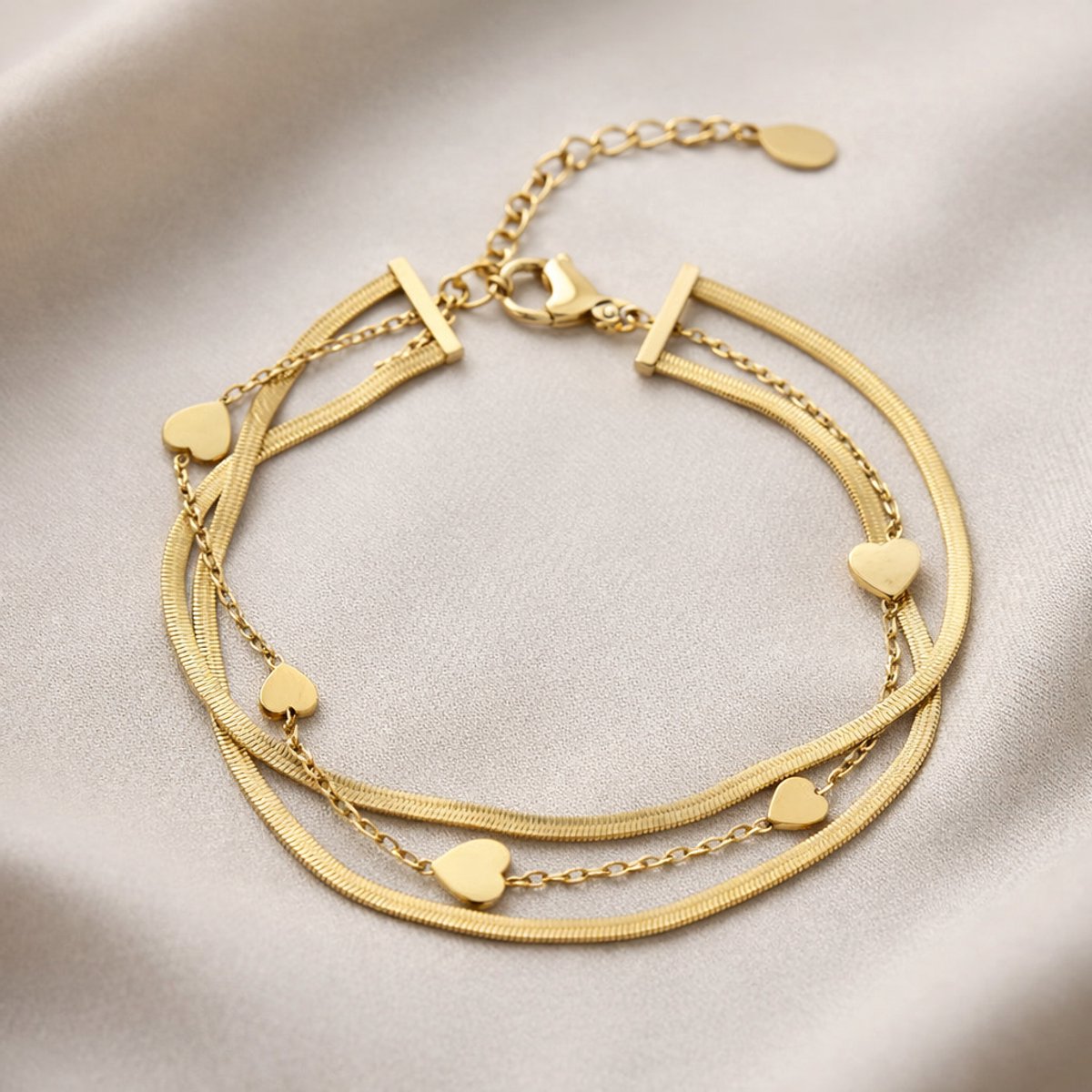 Lundholm My Yaar goudkleurige meerdere lagen schakelarmband voor dames van 16,4 cm met snake chain en hartjes accenten, gefotografeerd op crème zijde voor elegante productshot. Premium stainless steel met PVD gold plating van 2.5 micron, waterproof en hypoallergeen. Een romantisch cadeau voor vrouw, moeder of vriendin op Moederdag of verjaardag in Scandinavisch design.