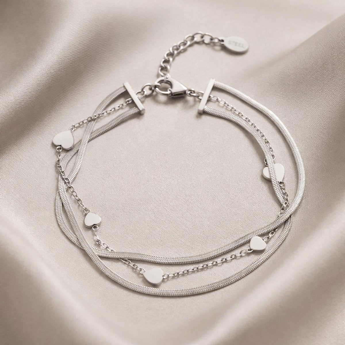 Lundholm My Yaar zilverkleurige meerdere lagen schakelarmband voor dames met snake chain en hartjes accenten, gefotografeerd op crème zijde voor elegante productshot. Premium stainless steel met PVD silver plating, waterproof en hypoallergeen. Een romantisch cadeau voor vrouw, moeder of vriendin op Moederdag of verjaardag in Scandinavisch design.