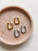 Lundholm MyKopenhagen Serie chunky geometrische oorbellen dames goudkleurig en zilverkleurig samen op roze marmeren schaal - waterproof gold plated PVD premium stainless steel sieraden cadeau vrouw moederdag verjaardag Scandinavisch Design