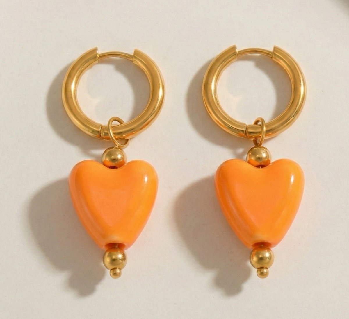Lundholm Neeltje goudkleurige huggie oorbellen voor dames met grote oranje hartjes hangers van 4 cm, perfect voor Koningsdag accessoires en feestelijke gelegenheden. Premium stainless steel met PVD gold plating van 2.5 micron, waterproof en hypoallergeen. Een vrolijk cadeau voor vrouw, moeder of vriendin op Koningsdag, Moederdag of verjaardag in Scandinavisch design.