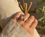 Lundholm Noe Serie luxe ring voor dames in goudkleurig met twee grote druppelvormige zirkonia stenen open design verstelbaar gedragen aan hand van model in lifestyle setting, gemaakt van premium stainless steel met PVD coating van 2.5 micron, waterproof en hypoallergeen, perfect cadeau voor vrouw, moederdag of verjaardag in Scandinavisch design.