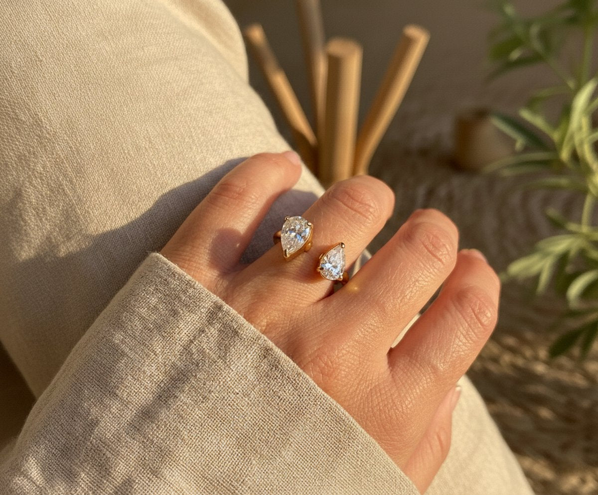 Lundholm Noe Serie luxe ring voor dames in goudkleurig met twee grote druppelvormige zirkonia stenen open design verstelbaar gedragen aan hand van model in lifestyle setting, gemaakt van premium stainless steel met PVD coating van 2.5 micron, waterproof en hypoallergeen, perfect cadeau voor vrouw, moederdag of verjaardag in Scandinavisch design.