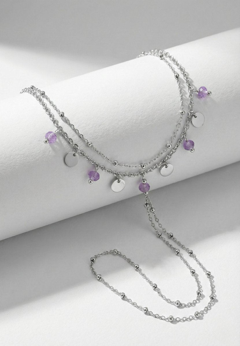 Lundholm Saar zilverkleurig handsieraad voor dames met hand chain ontwerp dat armband en ring verbindt, voorzien van paarse amethist en zilveren bedels, gefotografeerd op witte ondergrond voor stijlvolle productshot. Premium stainless steel met PVD silver plating, waterproof en hypoallergeen. Een uniek cadeau voor vrouw, moeder of vriendin op Moederdag of verjaardag in Scandinavisch design.