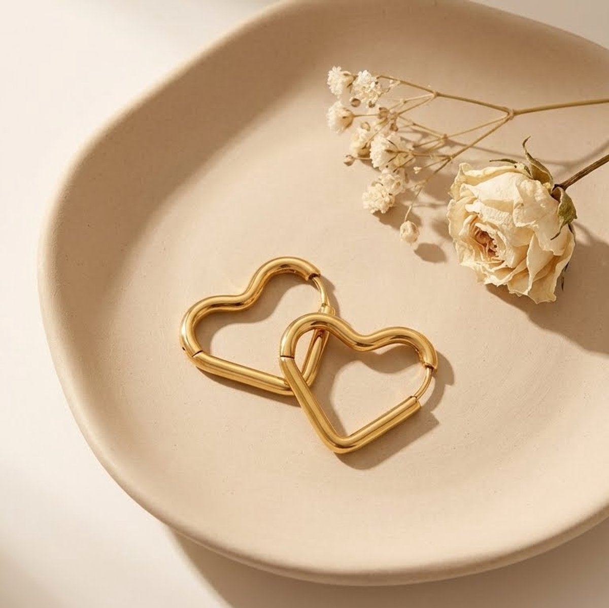 Lundholm Selma Serie hartje hoop oorbellen dames goudkleurig verguld op crème keramische schaal met witte droogbloemen lifestyle - waterproof gold plated PVD 2.5 micron premium stainless steel sieraden cadeau vrouw moederdag verjaardag Scandinavisch Design