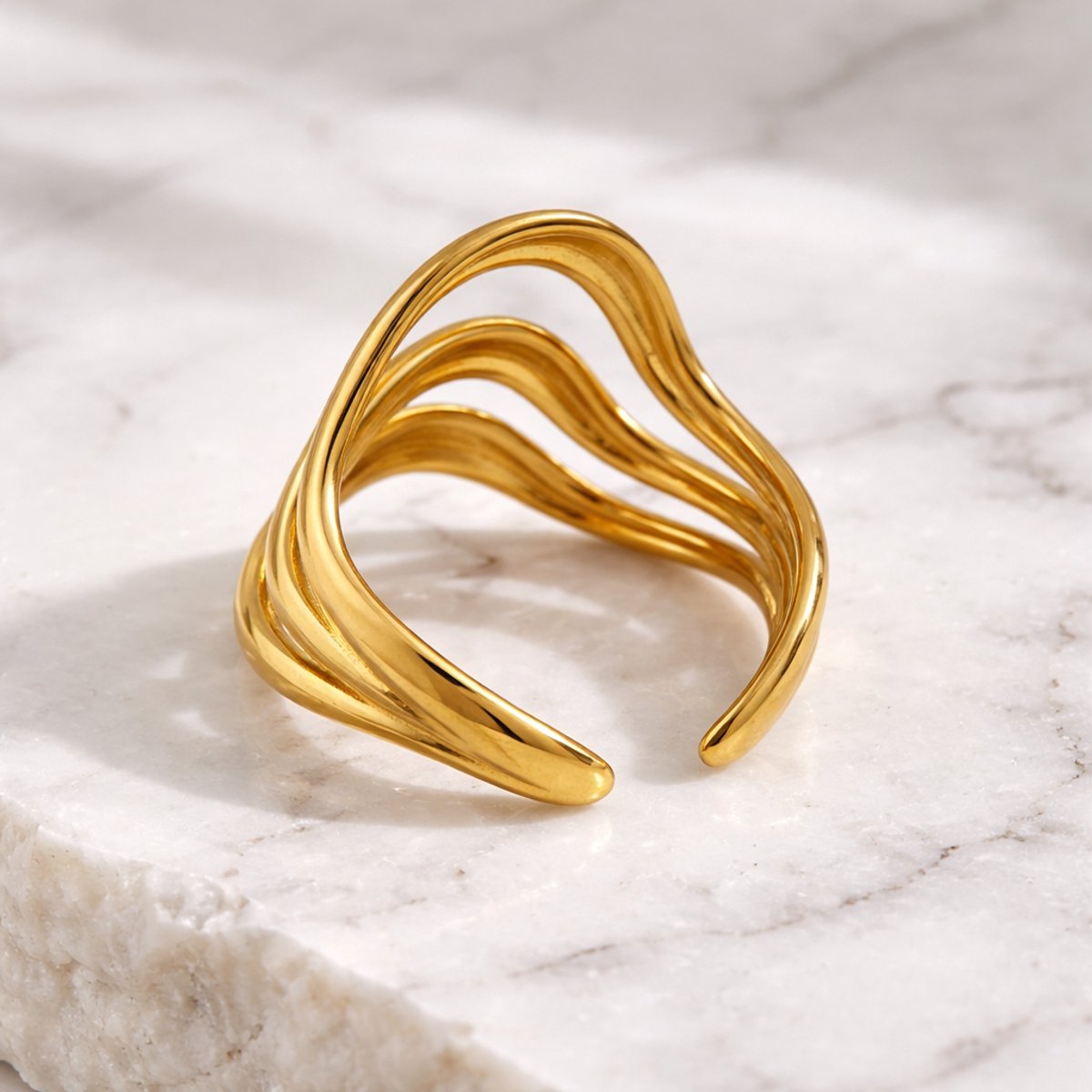 Lundholm Waves Serie luxe ring voor dames in goudkleurig met drie laags golvend design verstelbaar one size op marmeren ondergrond, gemaakt van premium stainless steel met PVD coating van 2.5 micron, waterproof en hypoallergeen, perfect cadeau voor vrouw, moederdag of verjaardag in Scandinavisch design.