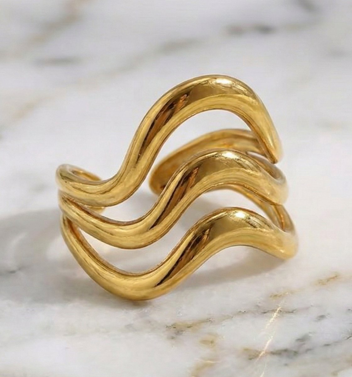Lundholm Waves Serie luxe ring voor dames in goudkleurig met drie laags golvend design verstelbaar one size op marmeren ondergrond, gemaakt van premium stainless steel met PVD coating van 2.5 micron, waterproof en hypoallergeen, perfect cadeau voor vrouw, moederdag of verjaardag in Scandinavisch design.