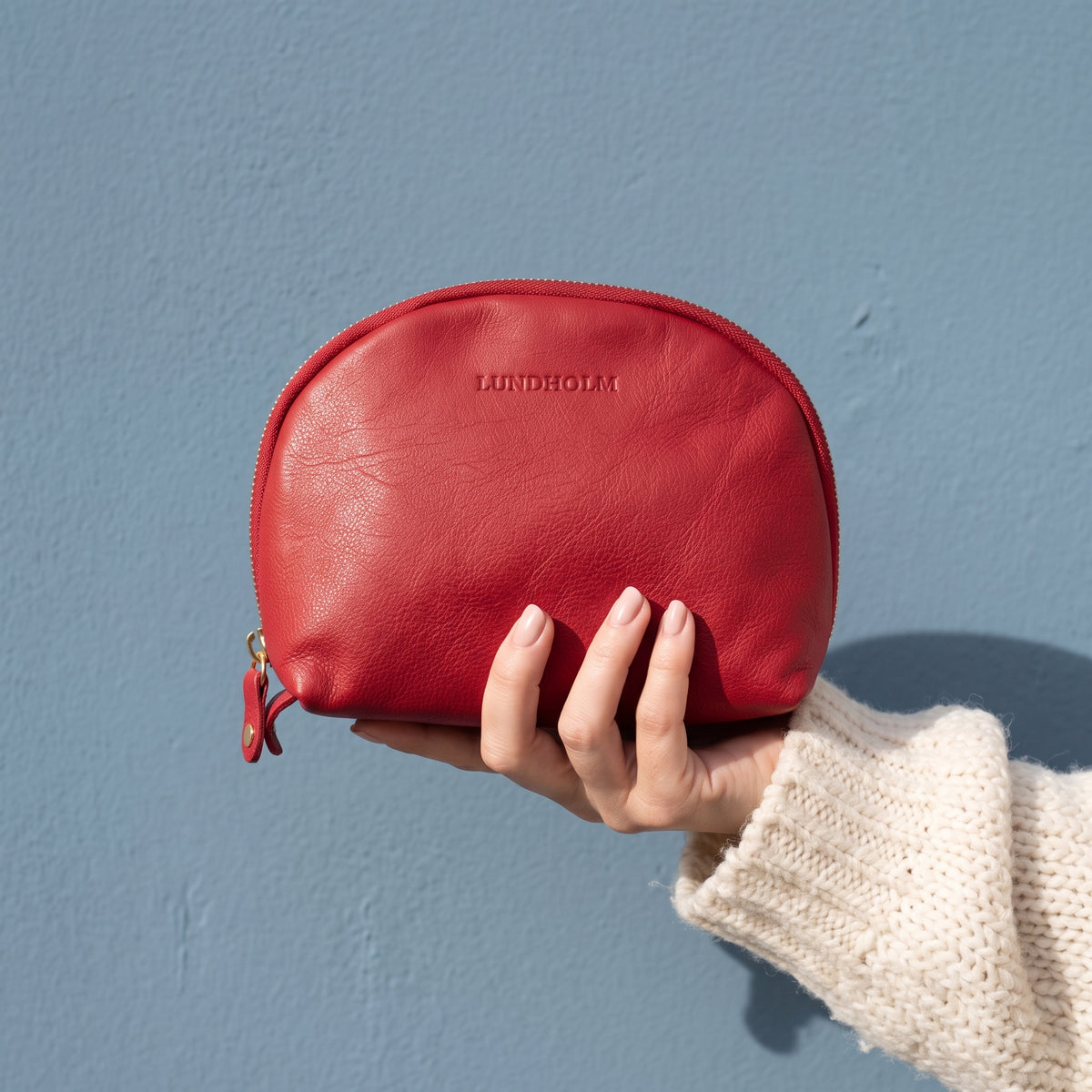 Lundholm make-up tasje rood van nappaleer in de hand, tegen een stoffig blauwe muur