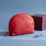 Lundholm half moon make-up tasje rood nappaleer met goudkleurige rits, naast een pruimkleurig blok