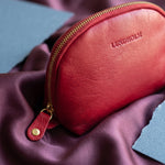 Detail van het Lundholm make-up tasje rood: LUNDHOLM-logo in het leer en goudkleurige rits op pruimkleurig satijn