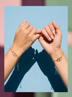 Twee handen doen een pinky promise met de Lundholm Alice armband met verstrengelde hartjes goudkleurig