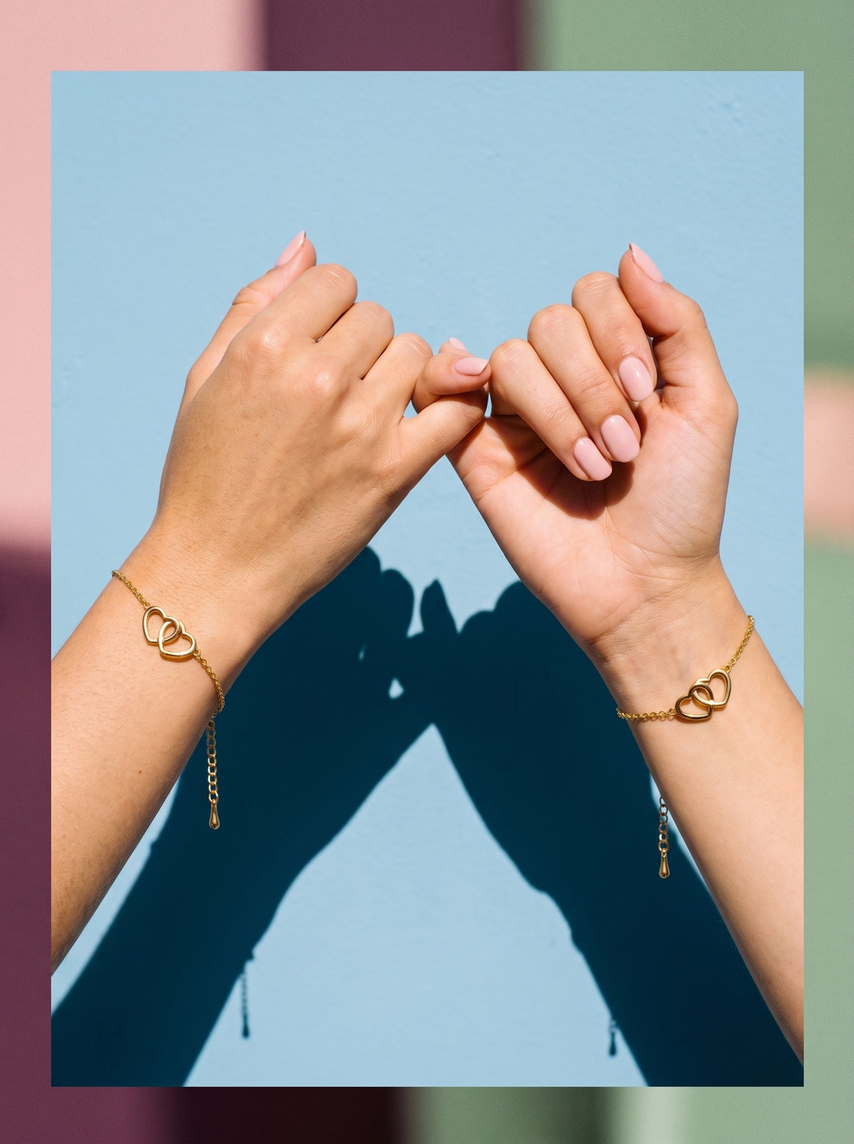 Twee handen doen een pinky promise met de Lundholm Alice armband met verstrengelde hartjes goudkleurig