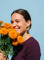 Vrouw met goudsbloemen draagt de Lundholm Aukje statement bloem oorbellen goudkleurig