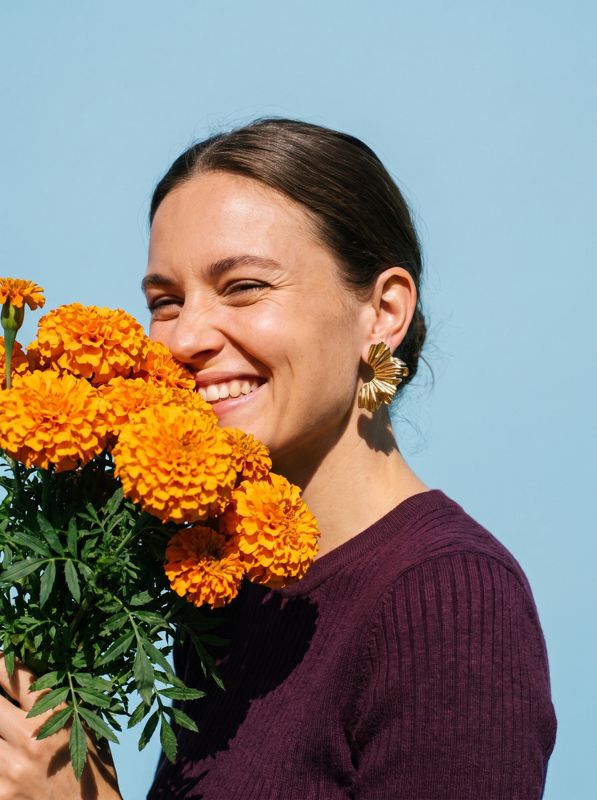 Vrouw met goudsbloemen draagt de Lundholm Aukje statement bloem oorbellen goudkleurig
