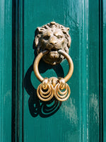 Lundholm Aura door knocker oorbellen goudkleurig aan een leeuwen deurklopper op een groene voordeur