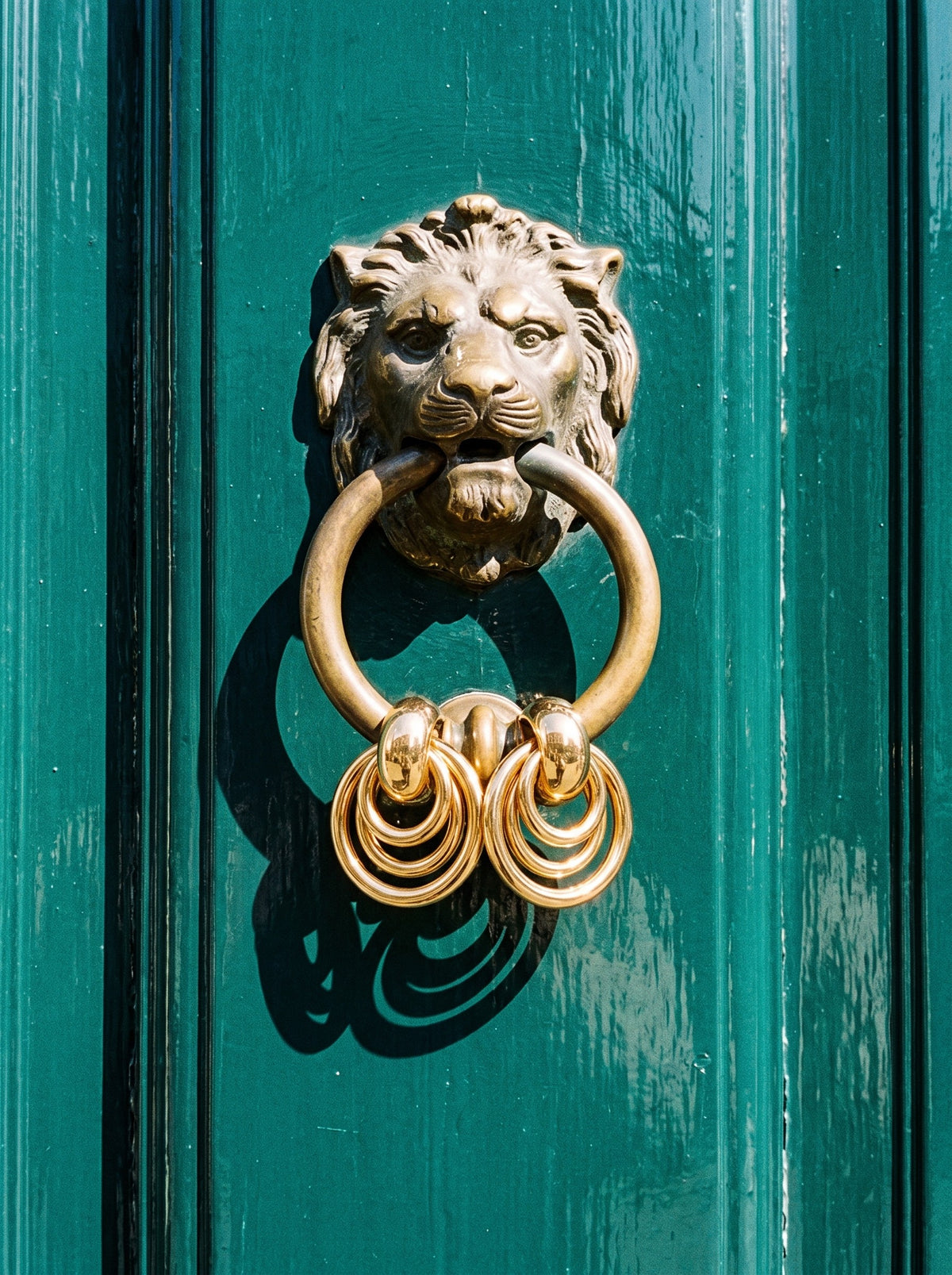 Lundholm Aura door knocker oorbellen goudkleurig aan een leeuwen deurklopper op een groene voordeur