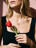Vrouw draagt de Lundholm Beryl ketting met open hart hanger goudkleurig, met een rode tulp