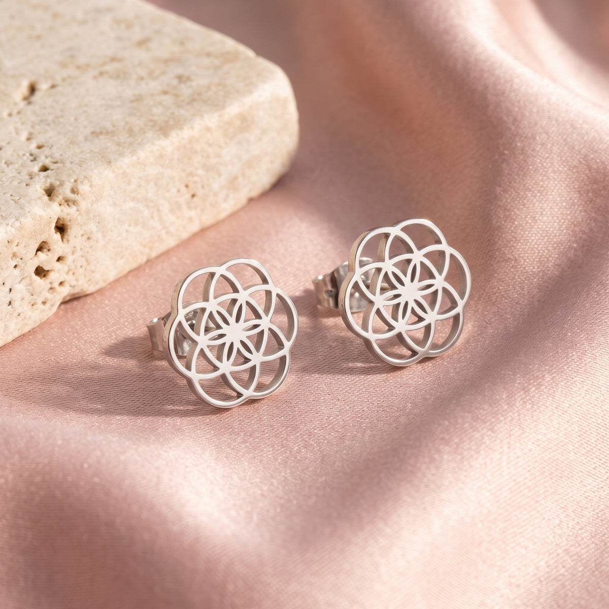Lundholm Pia oorknopjes zilver Bloem des Levens — flatlay op roze satijn en travertin