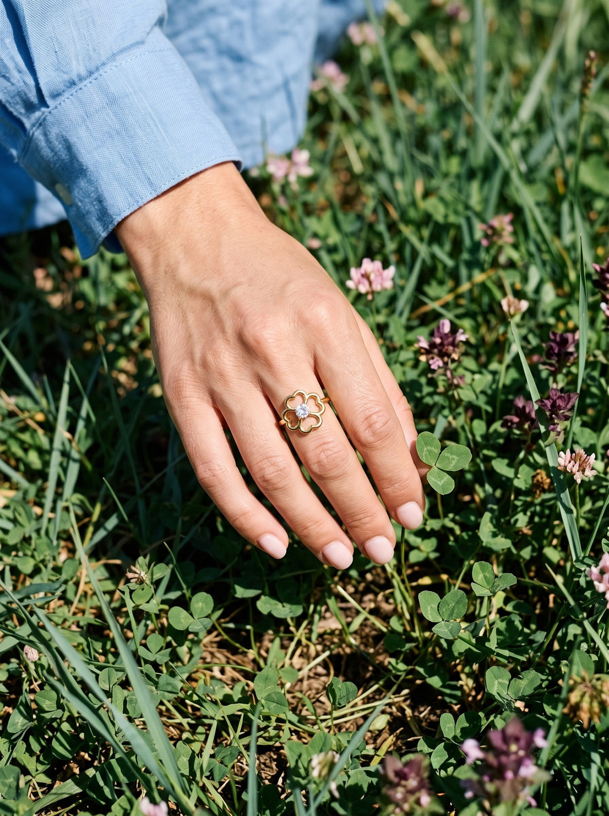 Hand met de Lundholm Bloom verstelbare klavertjevier ring goudkleurig tussen klaver in het gras