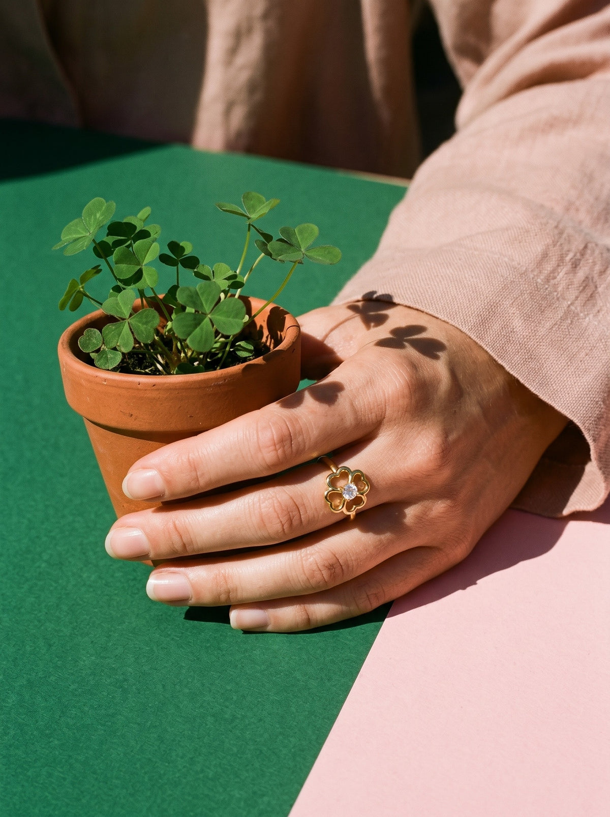 Lundholm Bloom klavertjevier ring met hartjes goudkleurig gedragen, hand om een klaverplantje