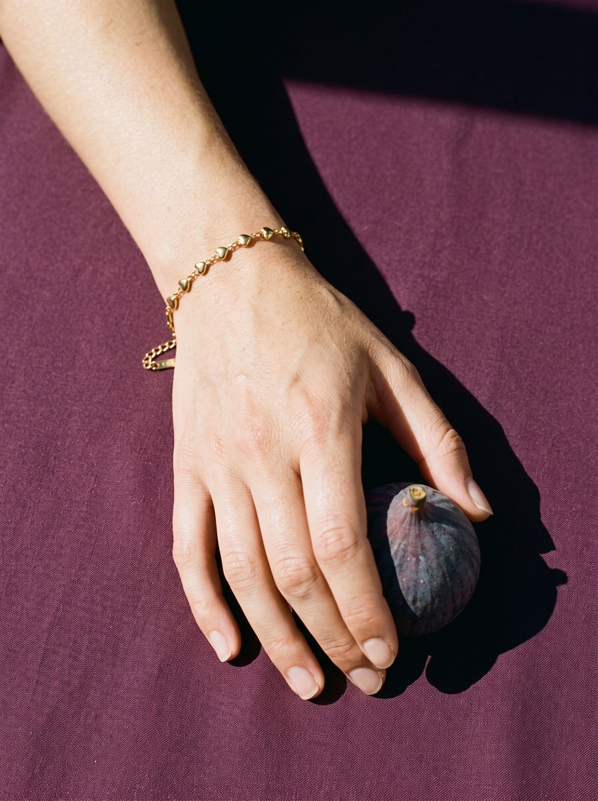 Hand met de Lundholm Britte minimalistische armband met hartjes goudkleurig en een verse vijg