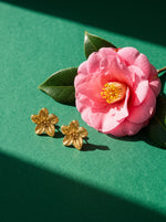 Lundholm Camellia bloem statement oorbellen goudkleurig naast een roze camelia