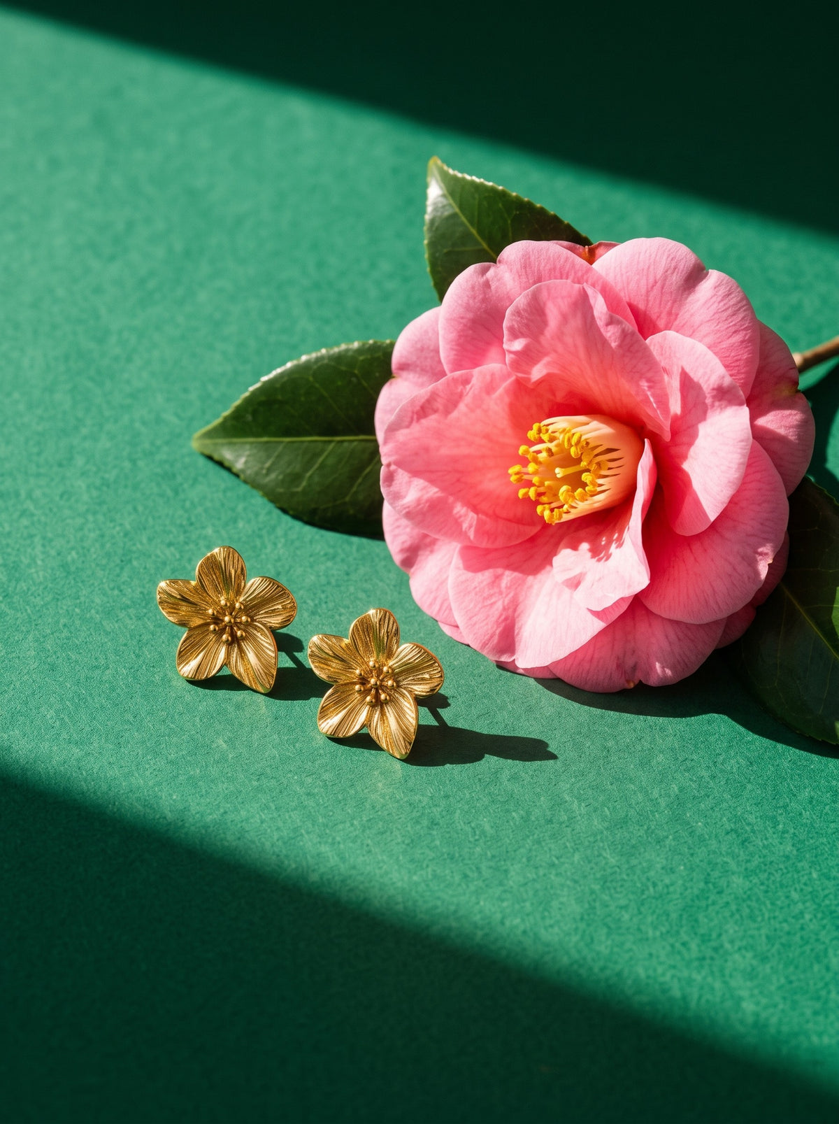 Lundholm Camellia bloem statement oorbellen goudkleurig naast een roze camelia