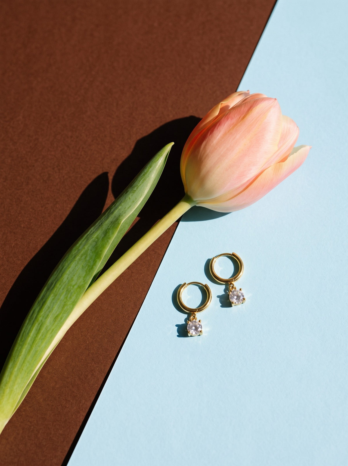 Lundholm Cathie huggie oorbellen met zirkonia hanger goudkleurig naast een perzikkleurige tulp