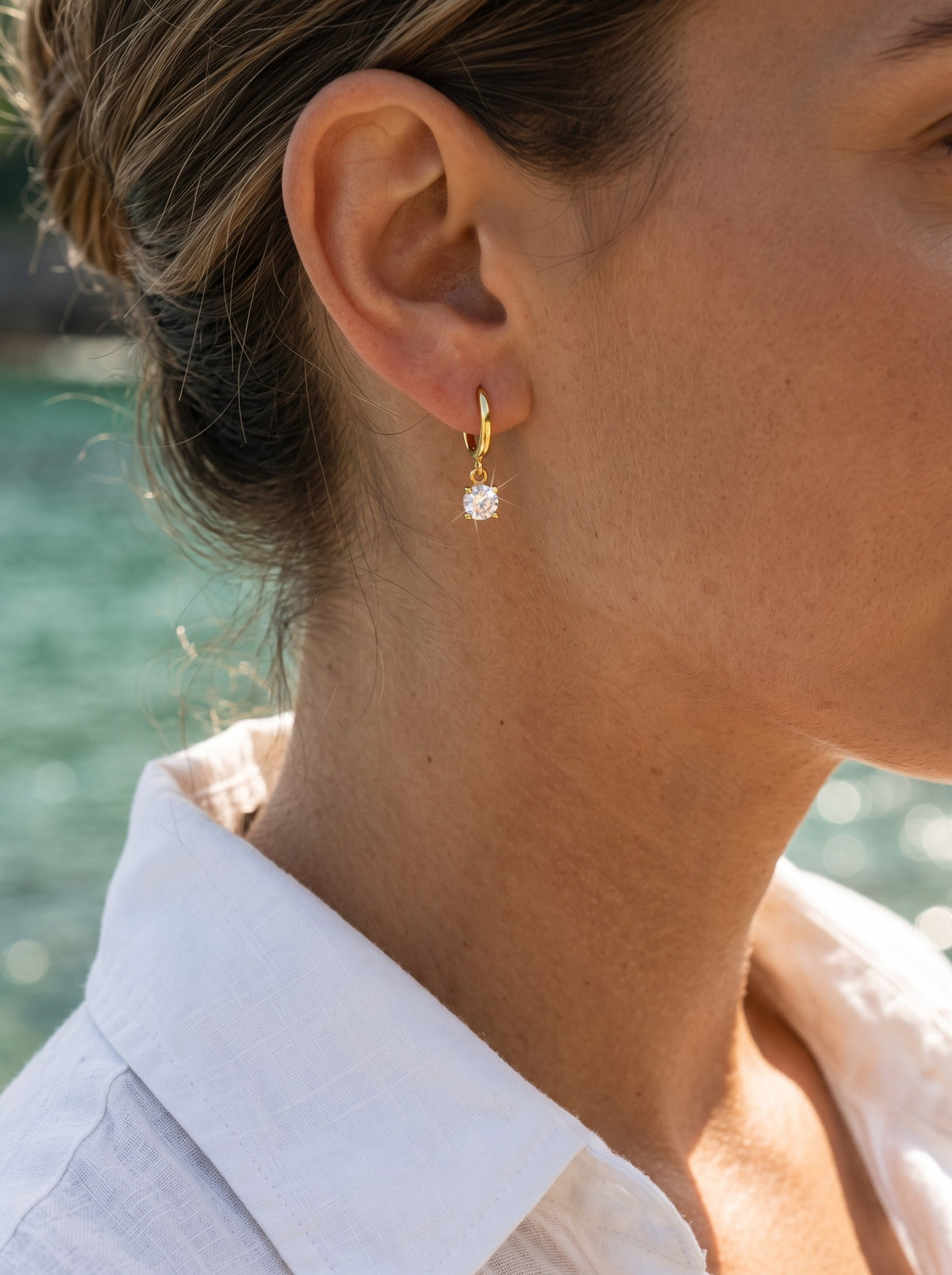 Vrouw in witte linnen blouse draagt de Lundholm Cathie huggie oorbellen met zirkonia hanger verguld