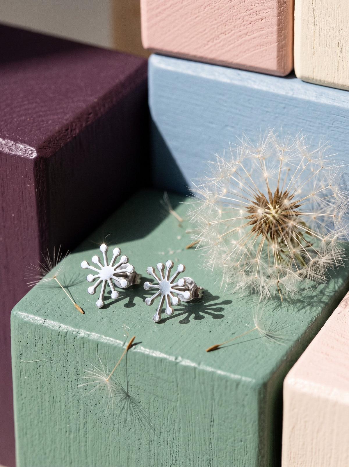 Lundholm Claudia paardenbloem oorknopjes zilverkleurig op pastel houten blokken naast een paardenbloem