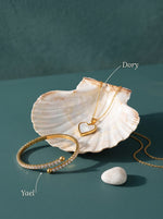 Lundholm Dory ketting met parelmoer hartje en Yael zirkonia tennisbangle goudkleurig in een sint-jakobsschelp