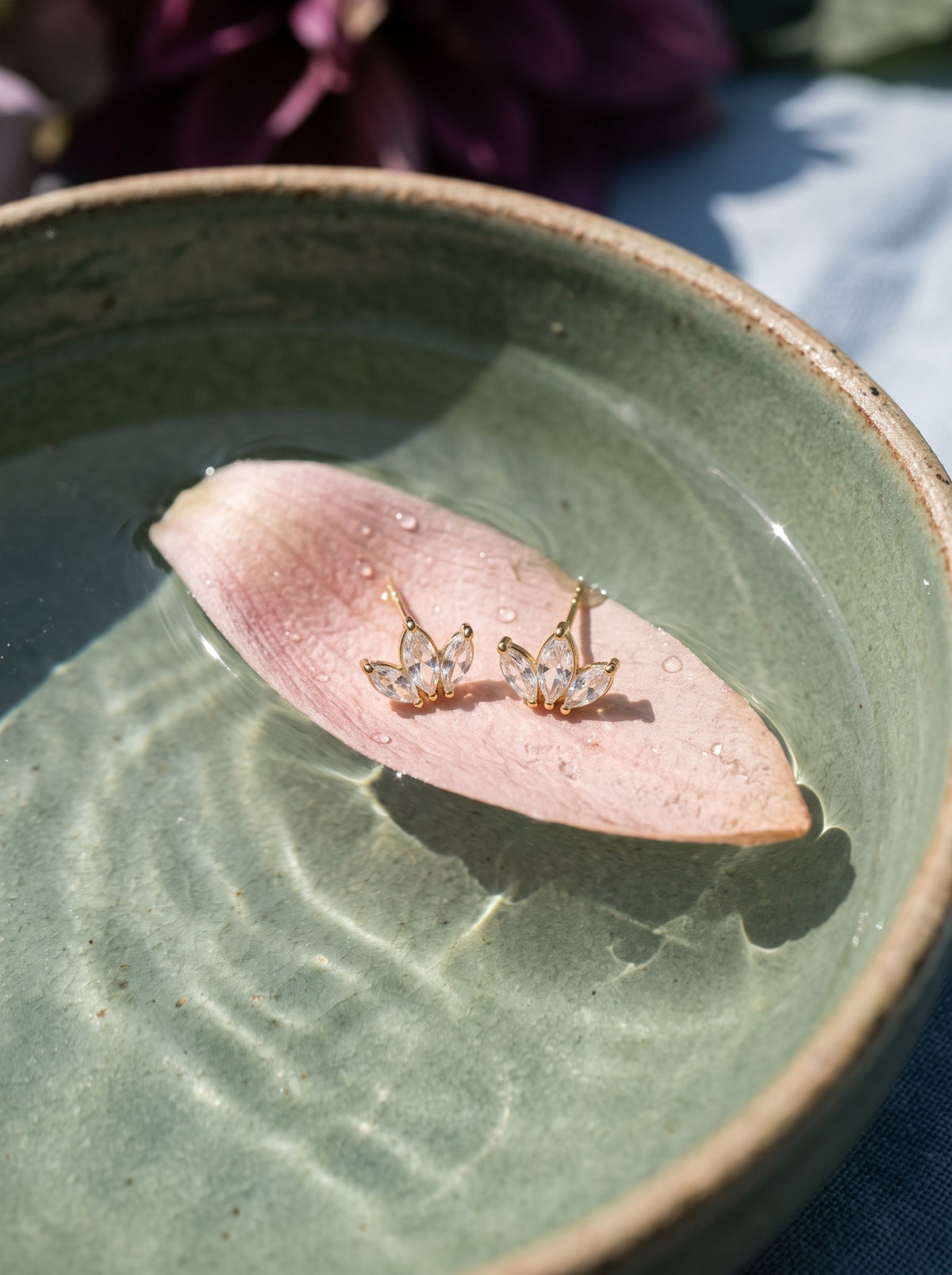 Lundholm Elara lotus oorknopjes met zirkonia goudkleurig op een roze bloemblad in een zeegroene schaal water