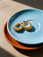 Lundholm Elin grote statement hoops goudkleurig op een lichtblauw schoteltje