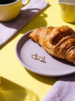 Lundholm Elska kleine hartjes oorknopjes goudkleurig op een lila bordje naast een croissant