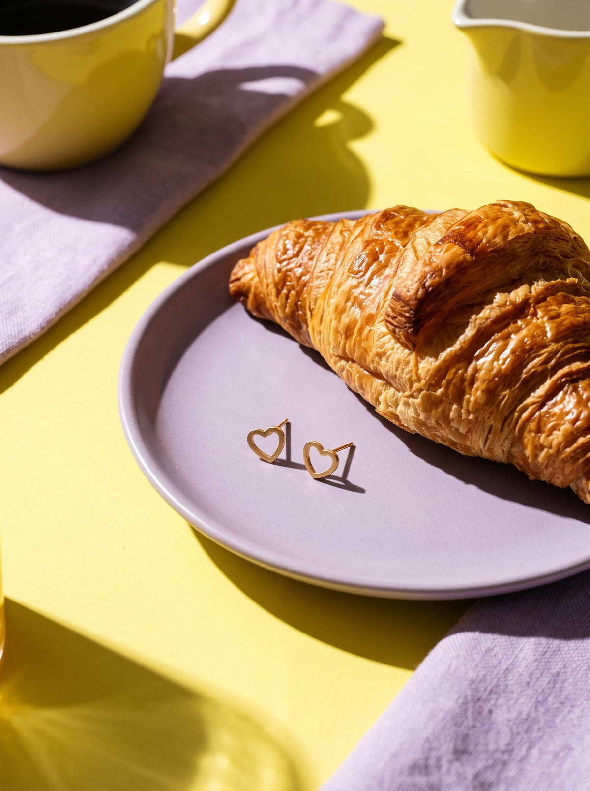 Lundholm Elska kleine hartjes oorknopjes goudkleurig op een lila bordje naast een croissant