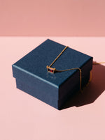 Lundholm Embla geboortesteen ketting goudkleurig met rode steen op een donkerblauw cadeaudoosje