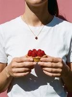 Vrouw in wit T-shirt draagt de Lundholm Emilia ketting met rood hartje goudkleurig, met een frambozentaartje