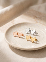 Lundholm Femme hartjes oorknopjes in goud, rosegoud en zilver op een keramieken schaaltje