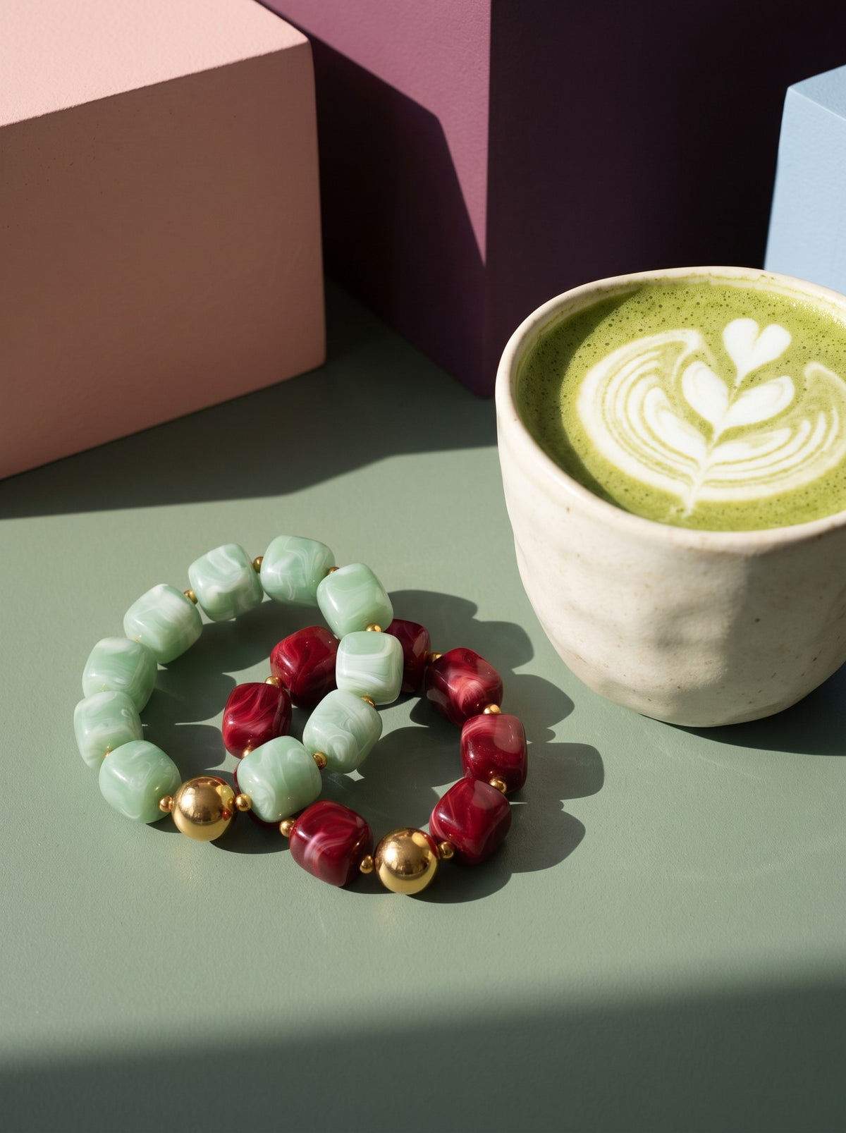 Lundholm Floor grote kralen armbanden in groen en rood met gouden kralen naast een matcha latte