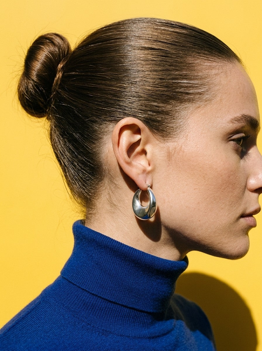 Vrouw in kobaltblauwe coltrui draagt de Lundholm Freyja statement hoops zilverkleurig