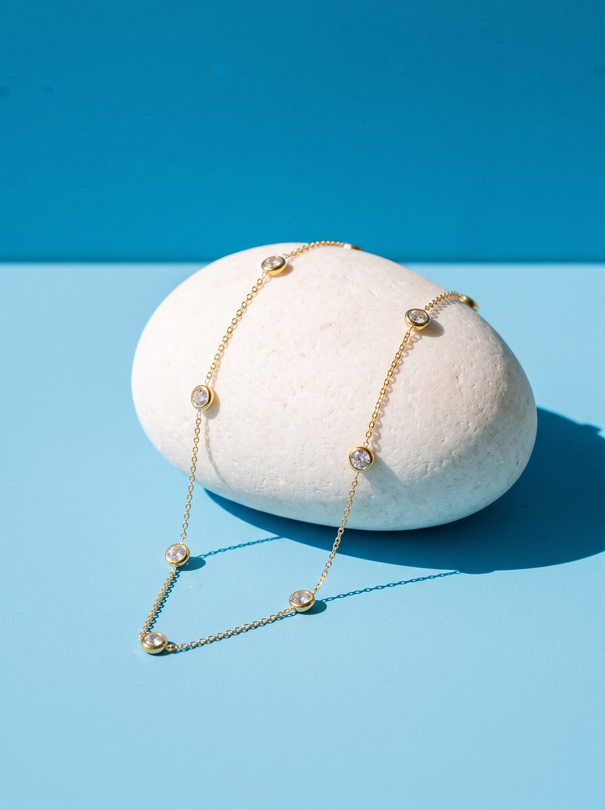 Lundholm Gigi ketting met witte zirkonia steentjes goudkleurig over een witte steen