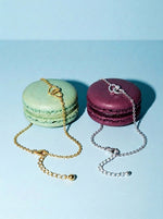 Goud en zilver combineren: de Lundholm Alice armband met verstrengelde hartjes in goudkleurig en zilverkleurig op een pistache- en een bramenmacaron