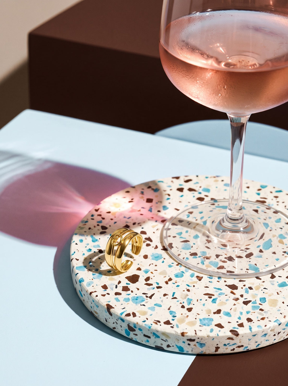 Lundholm Helena verstelbare infinity ring goudkleurig op een terrazzo onderzetter naast een glas rosé