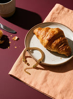 Lundholm Ilona schakelarmband goudkleurig op een perzikkleurig servet naast een croissant