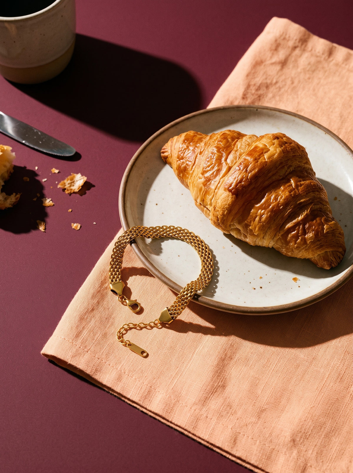 Lundholm Ilona schakelarmband goudkleurig op een perzikkleurig servet naast een croissant