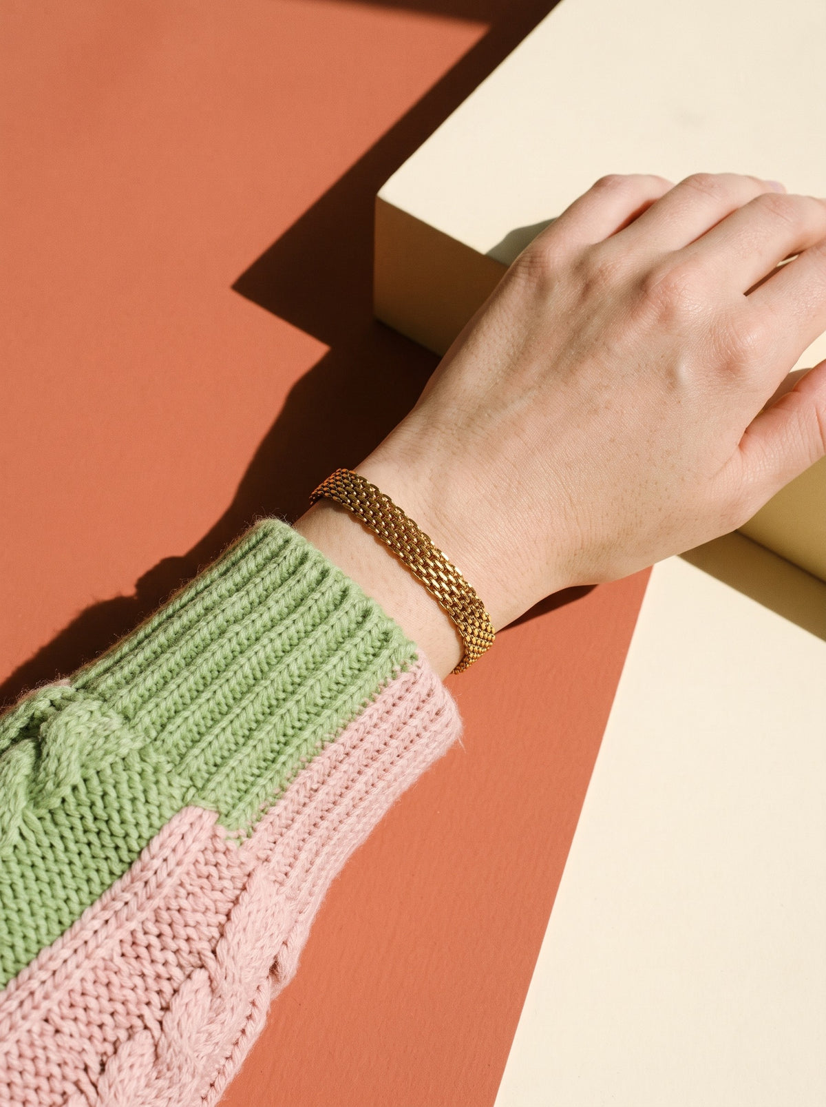 Pols met gebreide mouw draagt de Lundholm Ilona schakelarmband goudkleurig